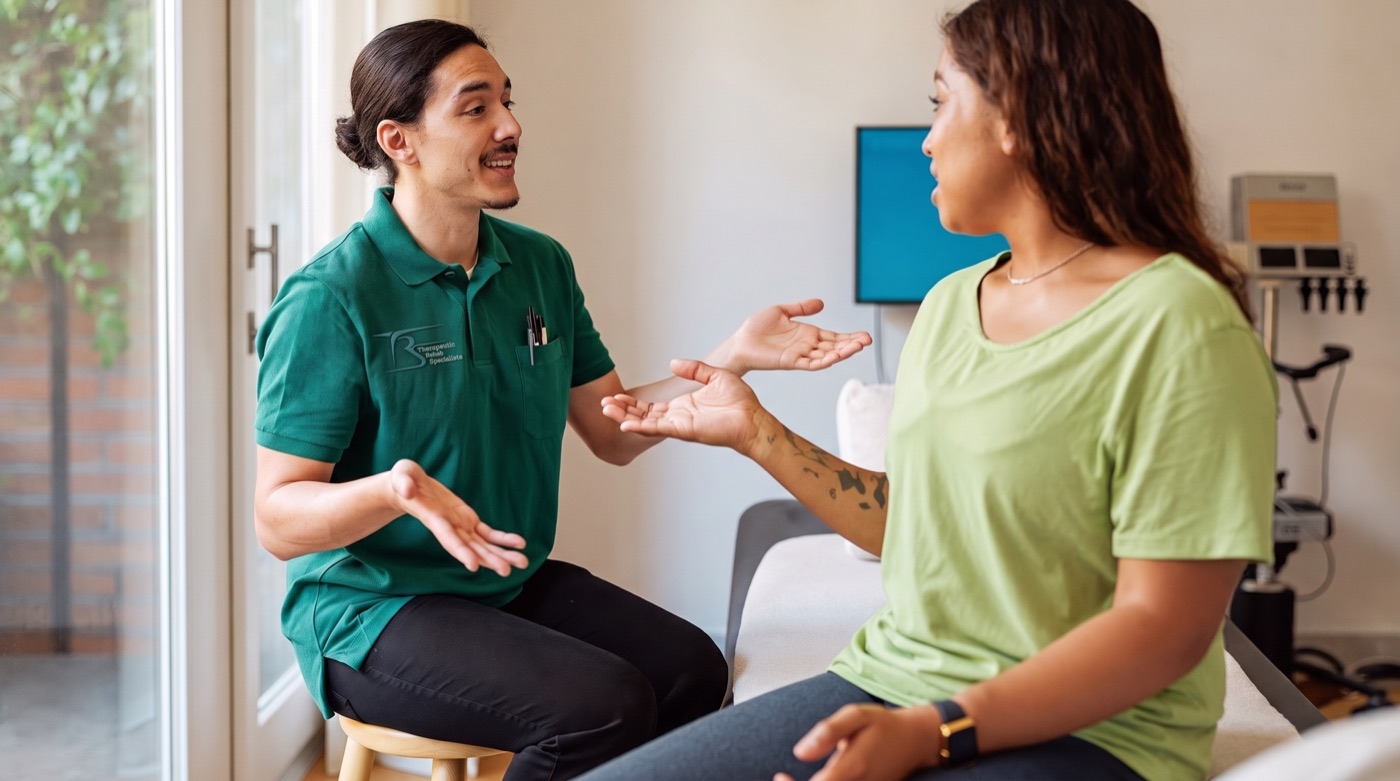 Physical therapist in a Therapeutic Rehab Specialists polo discussing treatment options with a patient